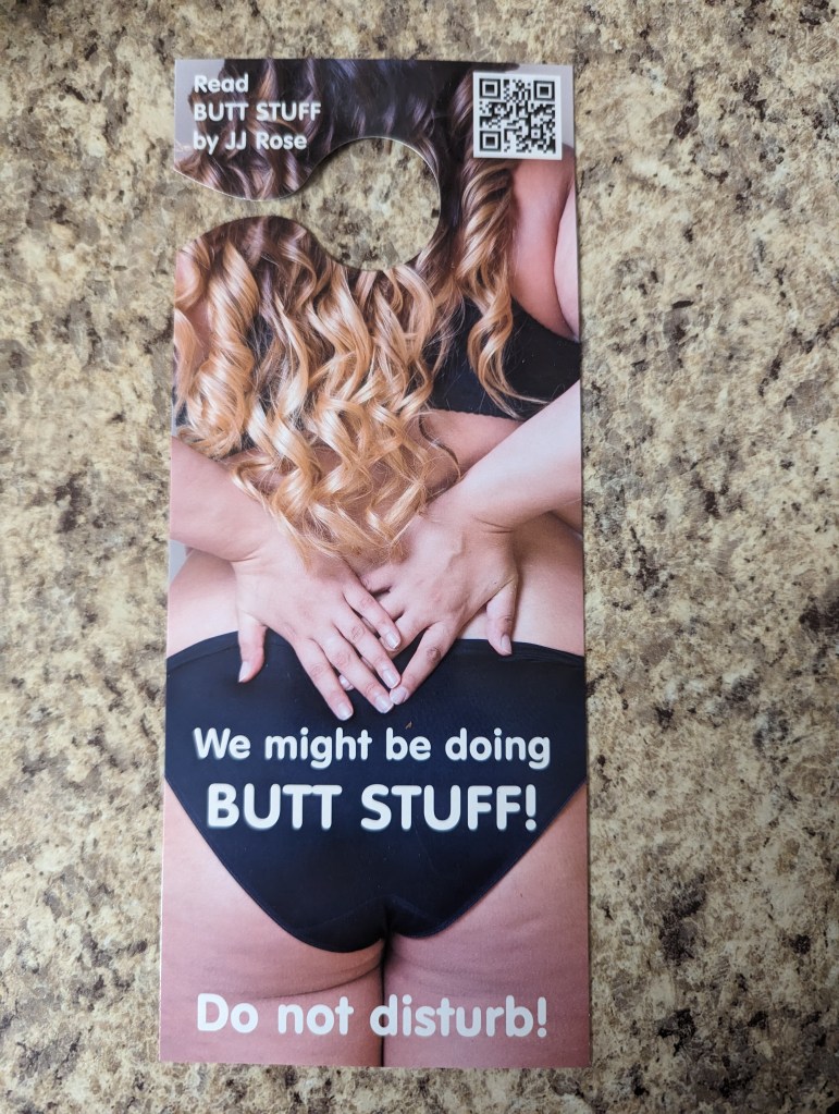 A door hanger, as one might find in a hotel room. The top-left corner says "Read BUTT STUFF by JJ Rose". The image is the back of a topless, curvy woman wearing black panties. On the panties it says "We might be doing BUTT STUFF!", and below that, "Do not disturb!"